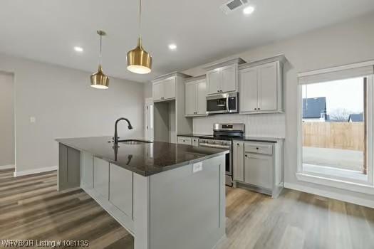 2018 Yellowstone Dr, Barling, AR 72903 - kitchen with appliances with stainless steel finishes, dark countertops, a sink, wood finished floors, and a center island with sink