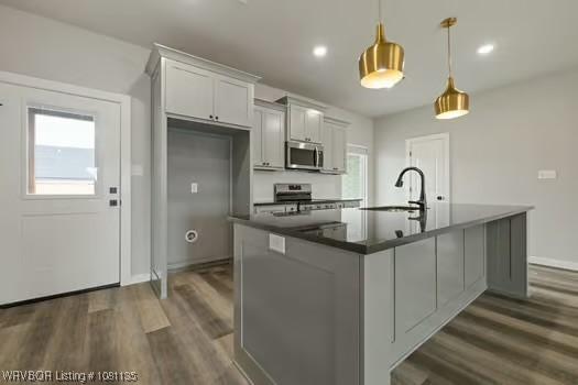 2018 Yellowstone Dr, Barling, AR 72903 - kitchen with stainless steel appliances, a sink, dark wood-style flooring, dark countertops, and an island with sink