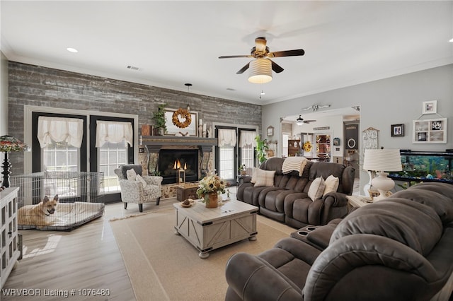 living room with wood walls, a stone fireplace, crown molding, ceiling fan, and light wood-type flooring