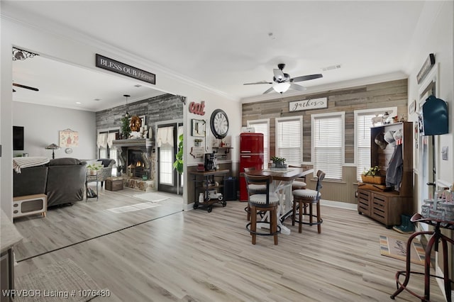 dining space featuring ceiling fan, light wood-type flooring, ornamental molding, and wooden walls