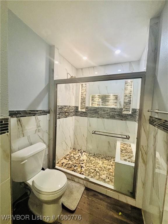 bathroom with toilet, wood finished floors, a wainscoted wall, tile walls, and a shower stall