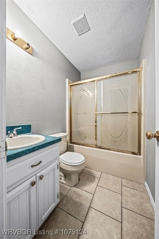 bathroom with a textured ceiling, tile patterned flooring, vanity, visible vents, and combined bath / shower with glass door