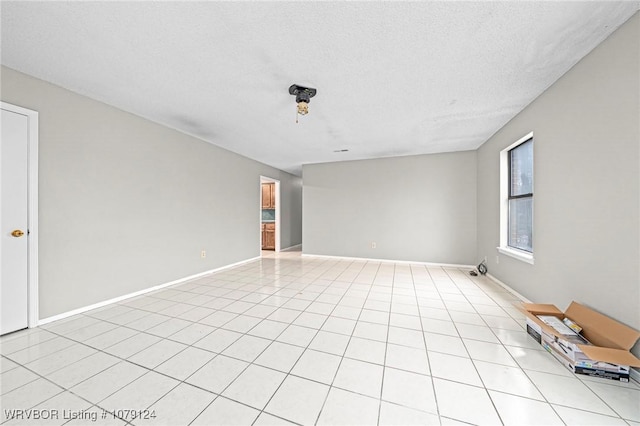 empty room featuring a textured ceiling, light tile patterned floors, and baseboards