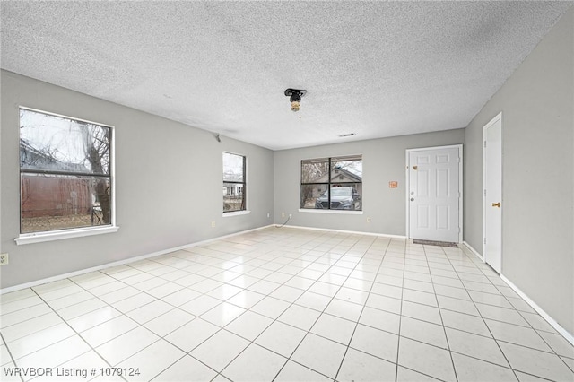 empty room with a textured ceiling, light tile patterned flooring, and baseboards