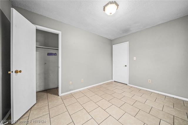 unfurnished bedroom featuring a closet, a textured ceiling, baseboards, and light tile patterned floors