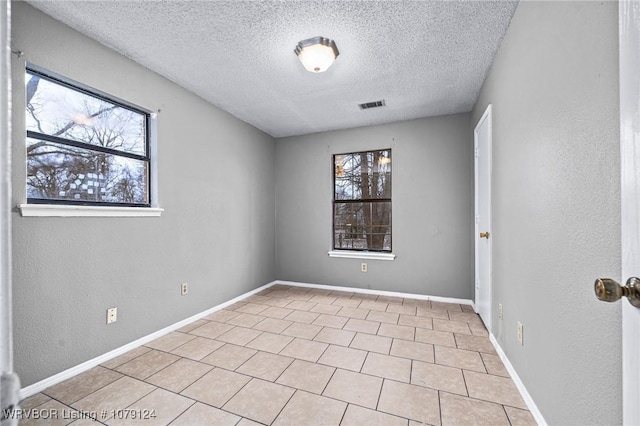 unfurnished room featuring baseboards, visible vents, a textured wall, a textured ceiling, and light tile patterned flooring