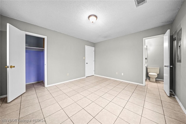 unfurnished bedroom featuring light tile patterned floors, a textured ceiling, visible vents, baseboards, and a closet