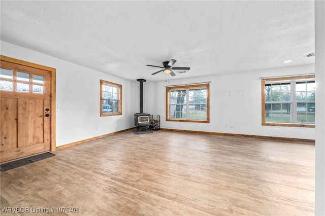 unfurnished living room with ceiling fan, light wood-type flooring, and a wood stove