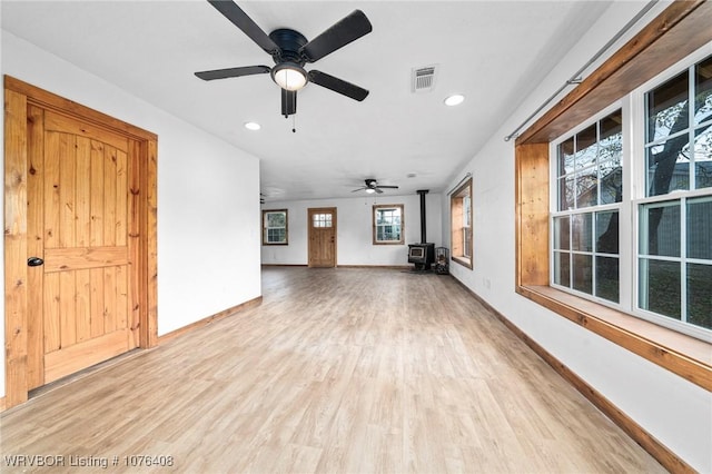 unfurnished living room featuring light hardwood / wood-style floors, a wood stove, and ceiling fan