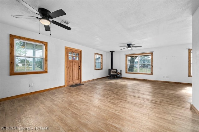 unfurnished living room featuring ceiling fan, a wood stove, a textured ceiling, and light hardwood / wood-style flooring