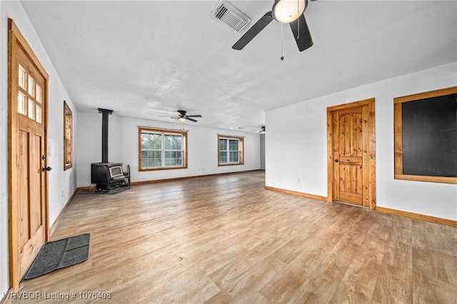 unfurnished living room with light hardwood / wood-style flooring, a wood stove, and ceiling fan