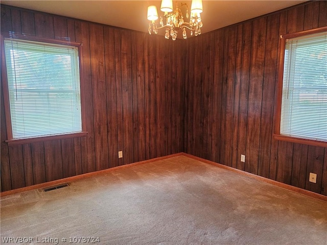 empty room featuring carpet flooring, a notable chandelier, and wood walls