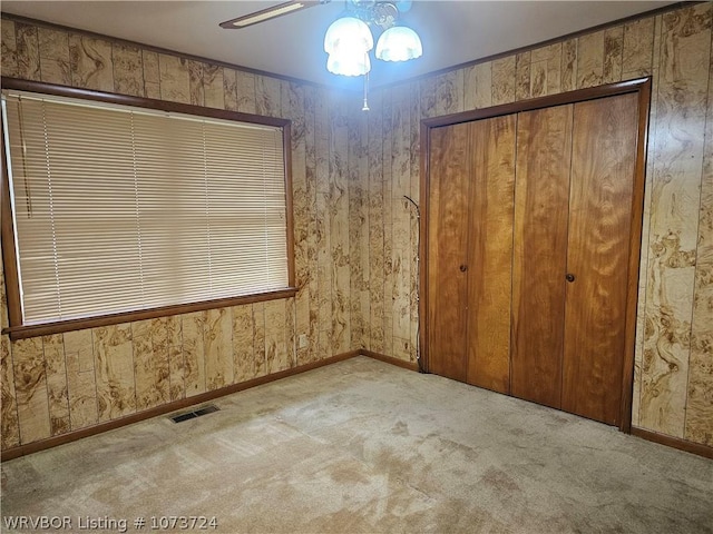 unfurnished bedroom featuring light carpet, a closet, wooden walls, and ceiling fan