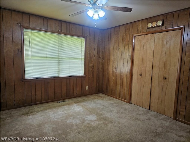 unfurnished bedroom with ceiling fan, light colored carpet, and wood walls