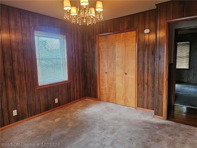 carpeted spare room featuring wood walls and a chandelier