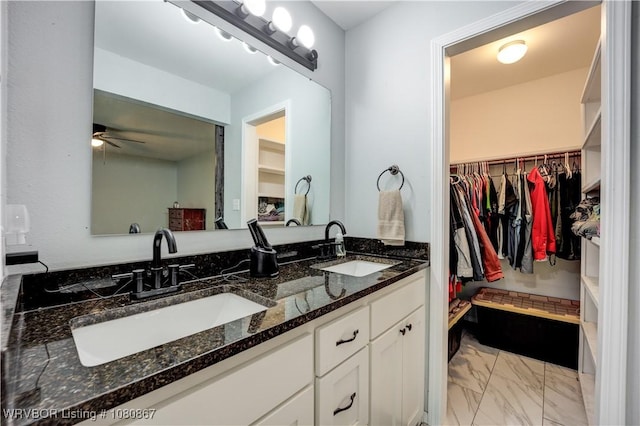 full bathroom with marble finish flooring, a spacious closet, a ceiling fan, and double vanity