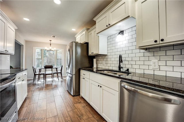 kitchen featuring appliances with stainless steel finishes, a sink, a chandelier, decorative backsplash, and white cabinets