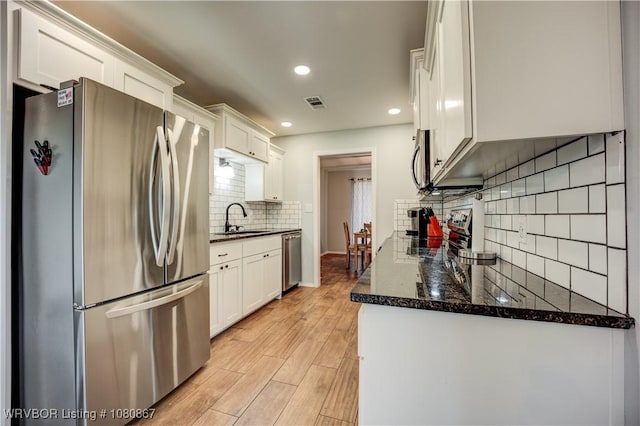 kitchen featuring stainless steel appliances, a sink, backsplash, white cabinetry, and light wood-type flooring