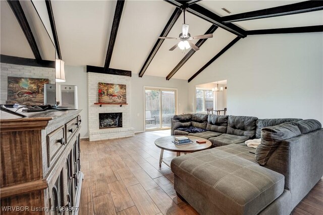 living room featuring a fireplace, a ceiling fan, beamed ceiling, light wood-type flooring, and a chandelier
