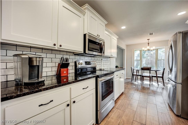 kitchen with stainless steel appliances, a chandelier, white cabinetry, decorative backsplash, and dark stone counters
