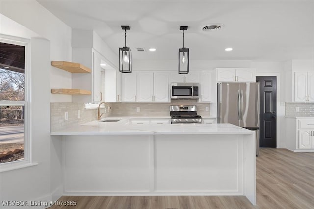 kitchen with pendant lighting, sink, white cabinets, kitchen peninsula, and stainless steel appliances