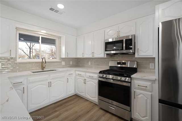 kitchen featuring sink, stainless steel appliances, white cabinets, and light stone countertops