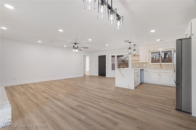 kitchen with white cabinets, backsplash, hanging light fixtures, stainless steel appliances, and light wood-type flooring