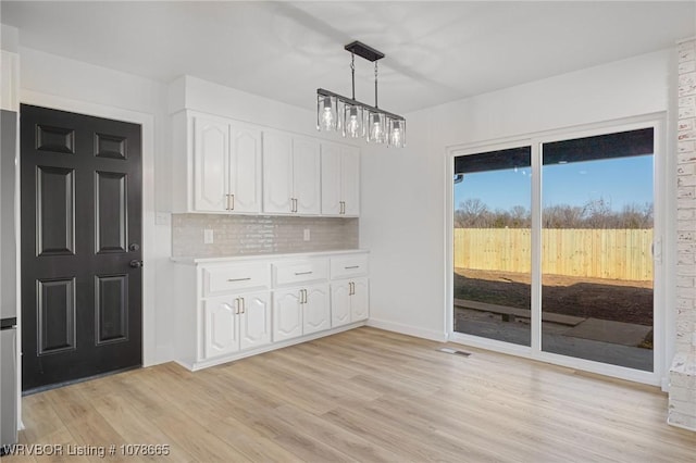 kitchen featuring hanging light fixtures, light wood-type flooring, white cabinets, a notable chandelier, and backsplash