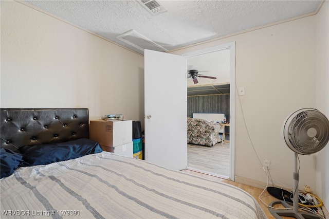 bedroom featuring a textured ceiling, wood finished floors, visible vents, and attic access