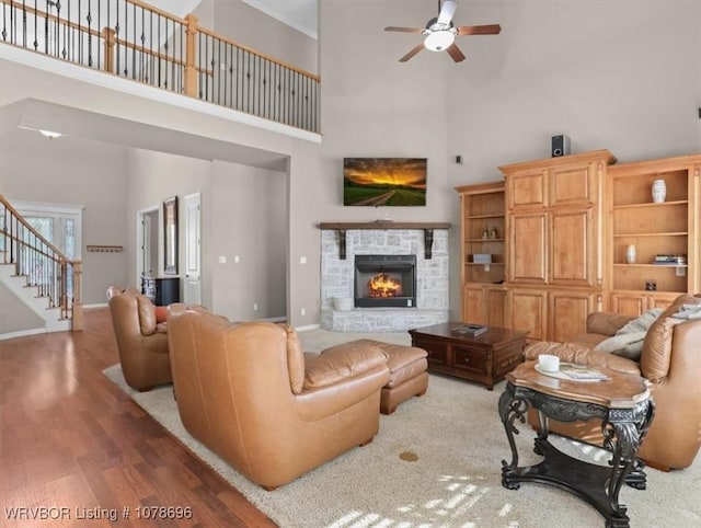 living room with ceiling fan, a fireplace, hardwood / wood-style floors, and a towering ceiling