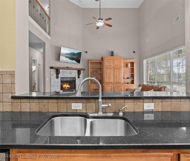 kitchen featuring ceiling fan, a towering ceiling, a stone fireplace, and sink