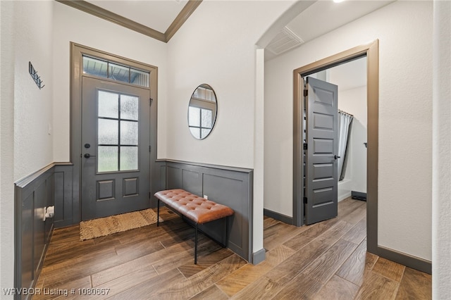 doorway with visible vents, arched walkways, wood finished floors, a wainscoted wall, and ornamental molding