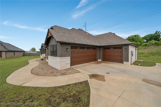 view of side of home featuring a yard, a shingled roof, concrete driveway, and stone siding