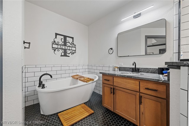 full bathroom featuring a freestanding bath, tile walls, tile patterned flooring, wainscoting, and vanity