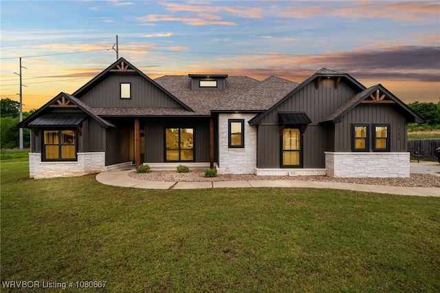 modern farmhouse style home with board and batten siding, roof with shingles, a front yard, and stone siding
