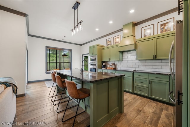 kitchen with crown molding, custom exhaust hood, a breakfast bar, green cabinetry, and appliances with stainless steel finishes
