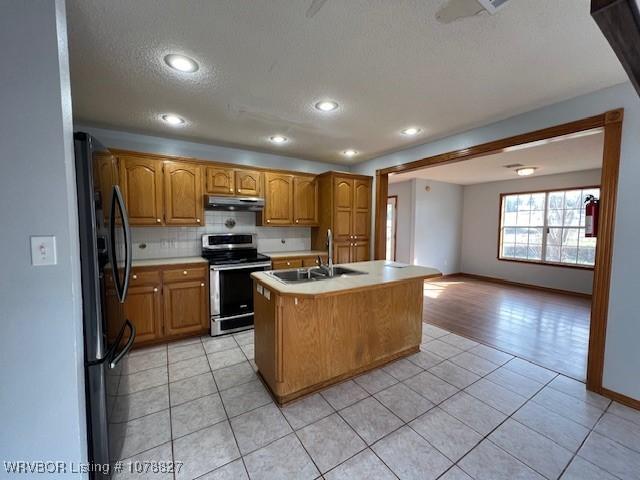 kitchen with a kitchen island with sink, sink, light tile patterned floors, and stainless steel appliances