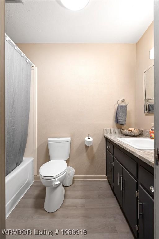 bathroom featuring baseboards, wood finished floors, toilet, vanity, and shower / bathtub combination with curtain