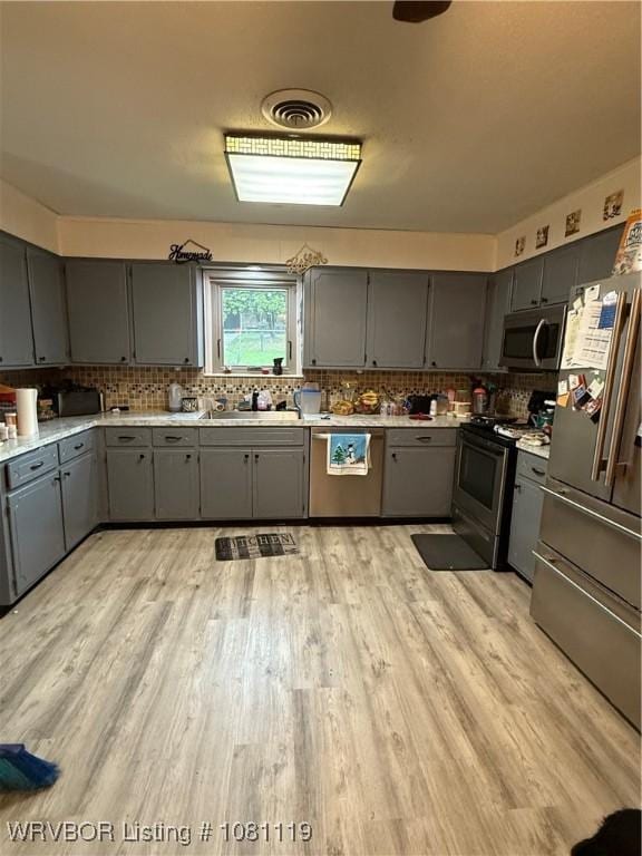 2303 Willow St, Van Buren, AR 72956 - kitchen with gray cabinetry, stainless steel appliances, light wood-style flooring, tasteful backsplash, and light countertops