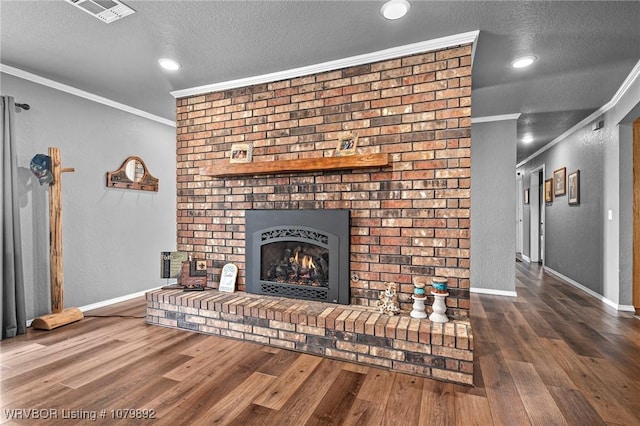 unfurnished living room featuring crown molding, wood finished floors, a textured ceiling, a brick fireplace, and visible vents