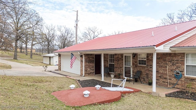 view of front of property with metal roof, a garage, brick siding, a front lawn, and a patio area