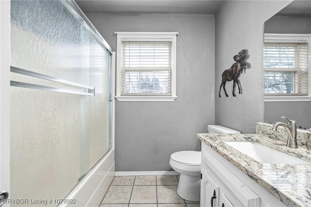 bathroom featuring vanity, shower / bath combination with glass door, toilet, baseboards, and tile patterned floors