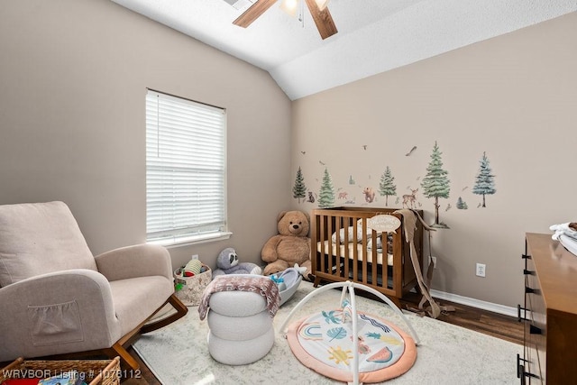 bedroom with wood-type flooring, vaulted ceiling, a nursery area, and ceiling fan