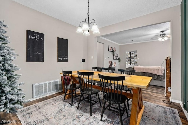 dining room with a textured ceiling, ceiling fan with notable chandelier, hardwood / wood-style flooring, and crown molding