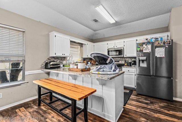 kitchen with white cabinetry, stainless steel appliances, a kitchen breakfast bar, kitchen peninsula, and a textured ceiling