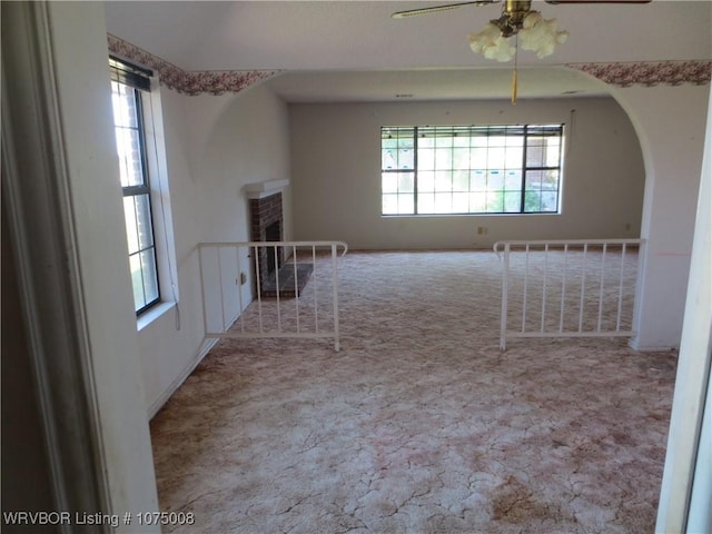 carpeted spare room with ceiling fan, a wealth of natural light, and a brick fireplace