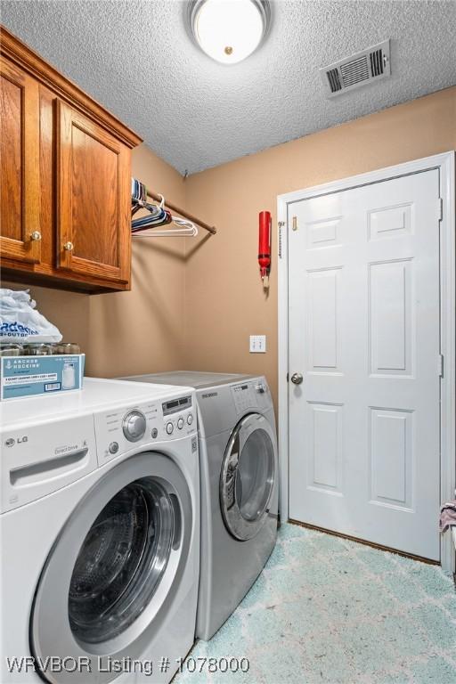 washroom with cabinets, a textured ceiling, and washing machine and dryer