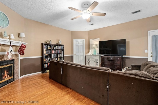 living room featuring ceiling fan, light hardwood / wood-style floors, a textured ceiling, and a tile fireplace