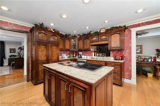 kitchen with a center island, sink, light stone counters, crown molding, and stainless steel gas stovetop