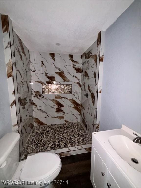 bathroom with a tile shower, vanity, and toilet